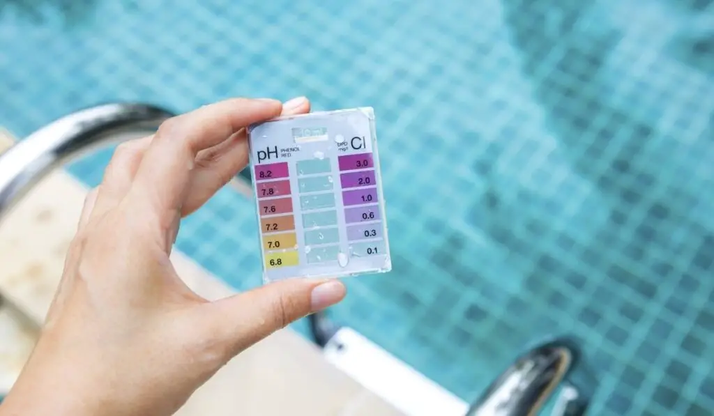 Girl hand holding mini water testing test kit over blurred swimming pool background 