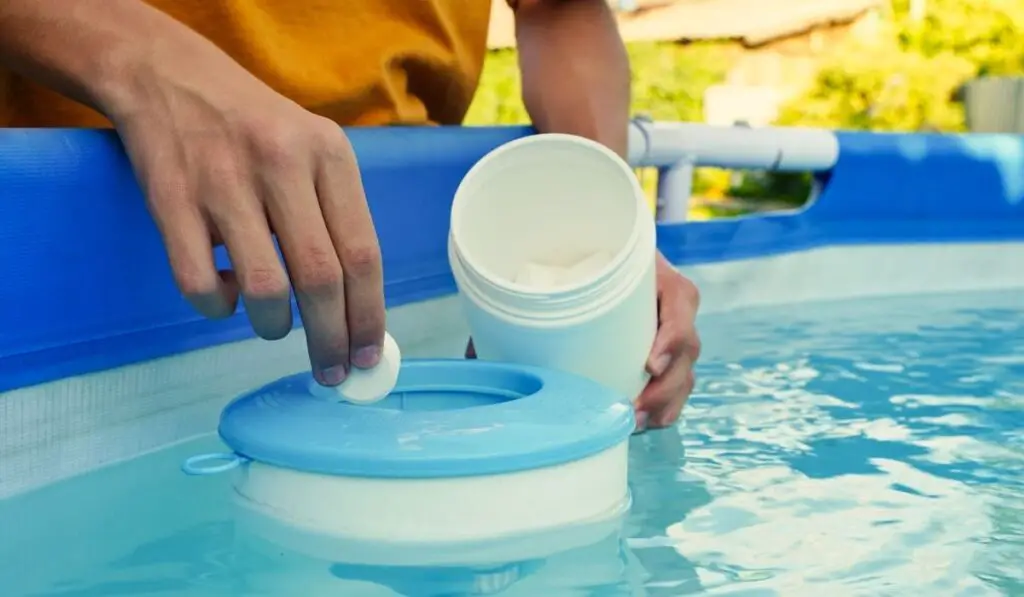 Hand holding white chlorine tablets over swimming pool skimmer 