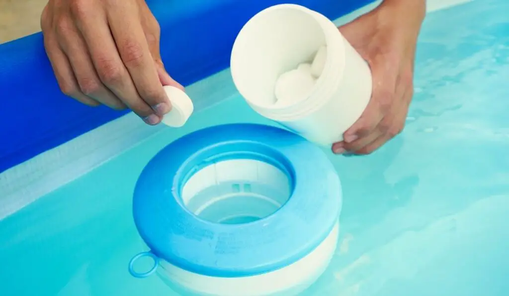 Hand holding white chlorine tablets over swimming pool skimmer