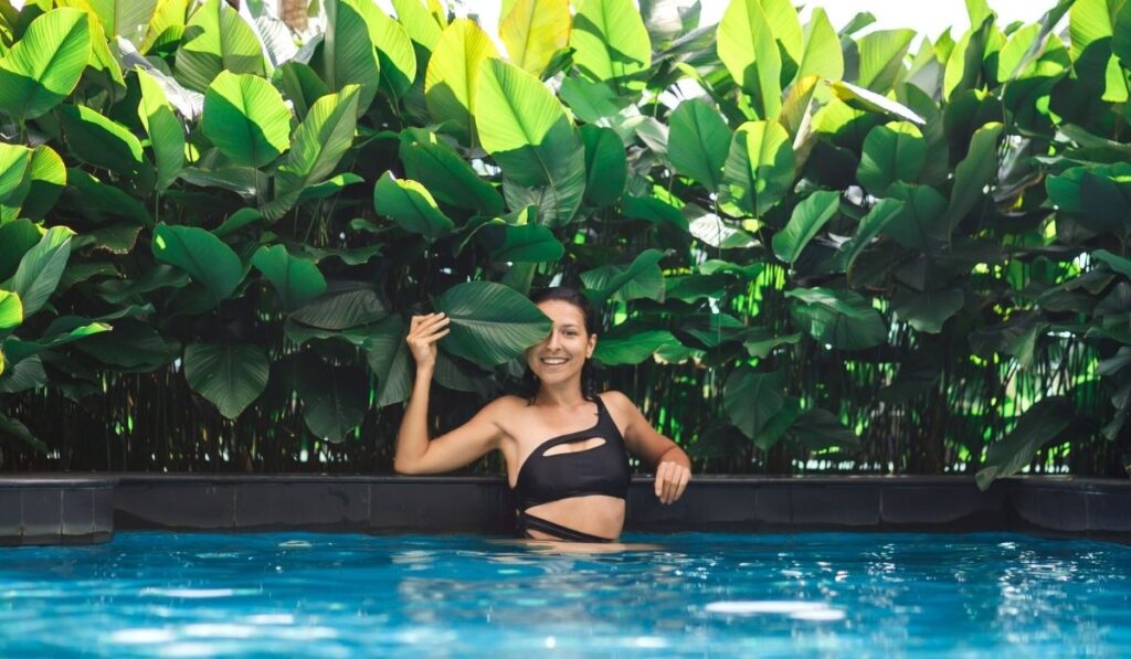 Portrait of young caucasian woman in swimming pool with green plants 