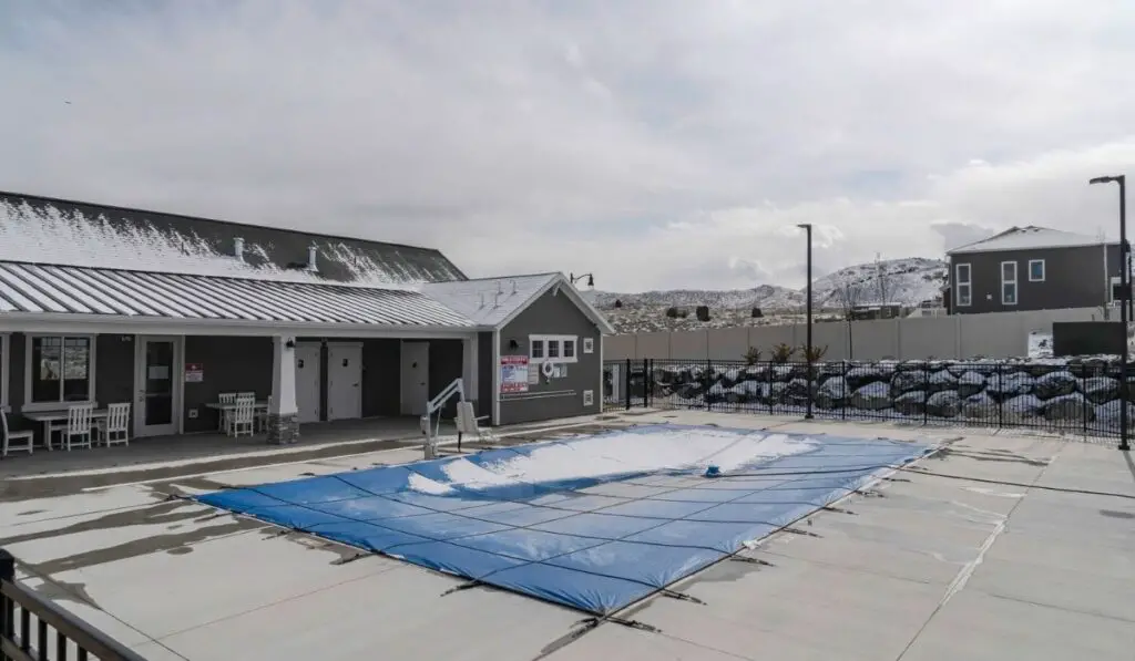 Swimming pool with plastic cover against snowy building houses and mountain