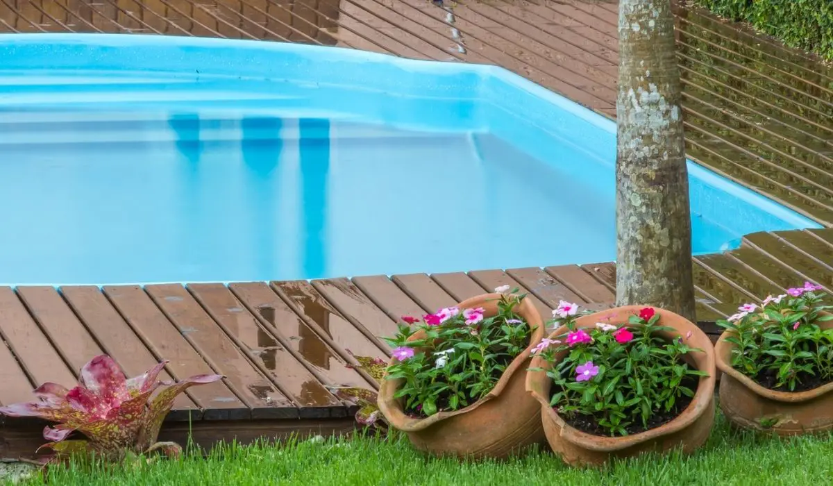 Backyard with a fiberglass pool on a wooden deck with flower pots and trees