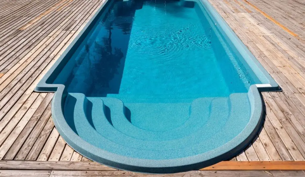 New modern fiberglass plastic swimming pool entrance step with clean fresh refreshing blue water on bright hot summer