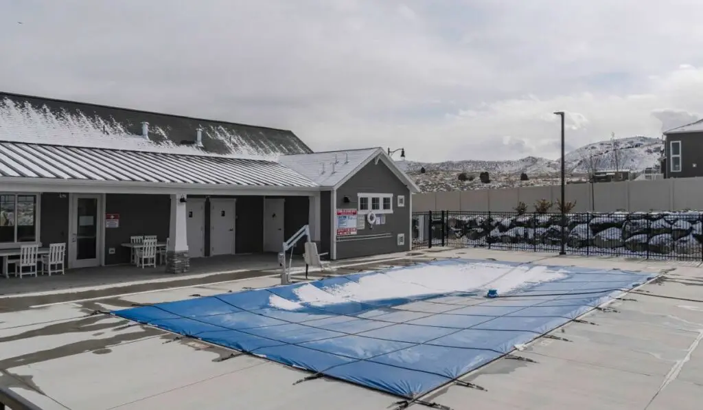 Swimming pool with plastic cover against snowy building houses and mountain