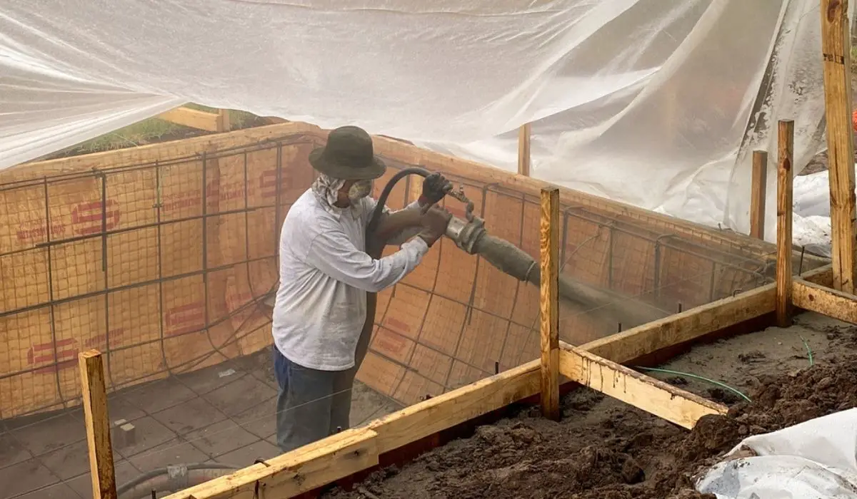 A construction worker spraying gunite on a swimming pool