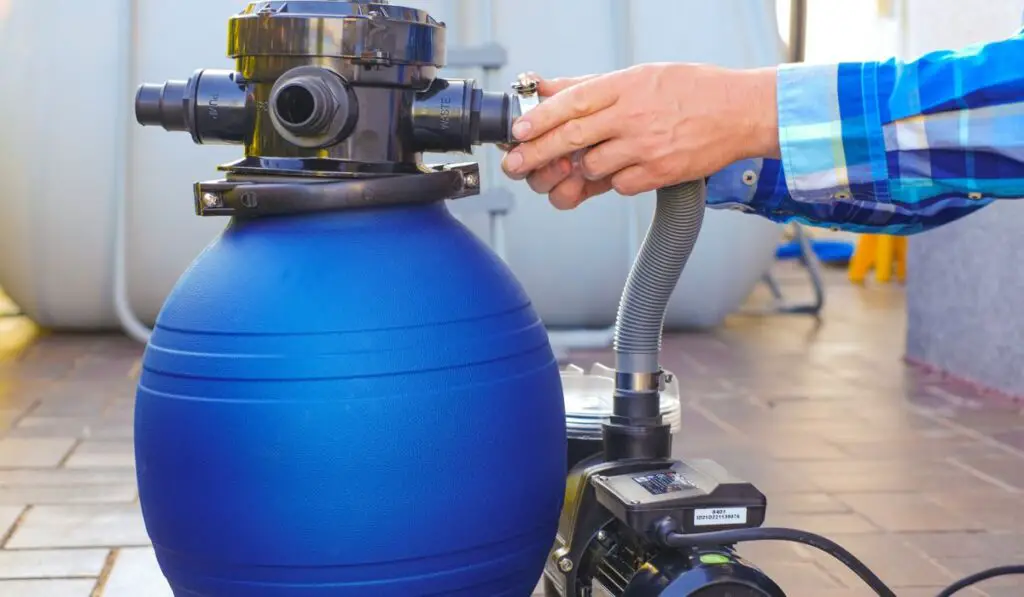 Blue water filter in the hands of a man in a blue shirt on terrace near the house 