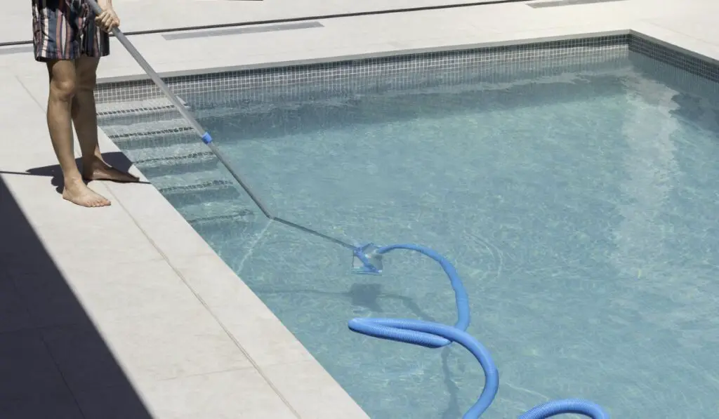 Faceless young man wearing swimwear using a machine to clean the bottom of a dirty swimming pool in summer 