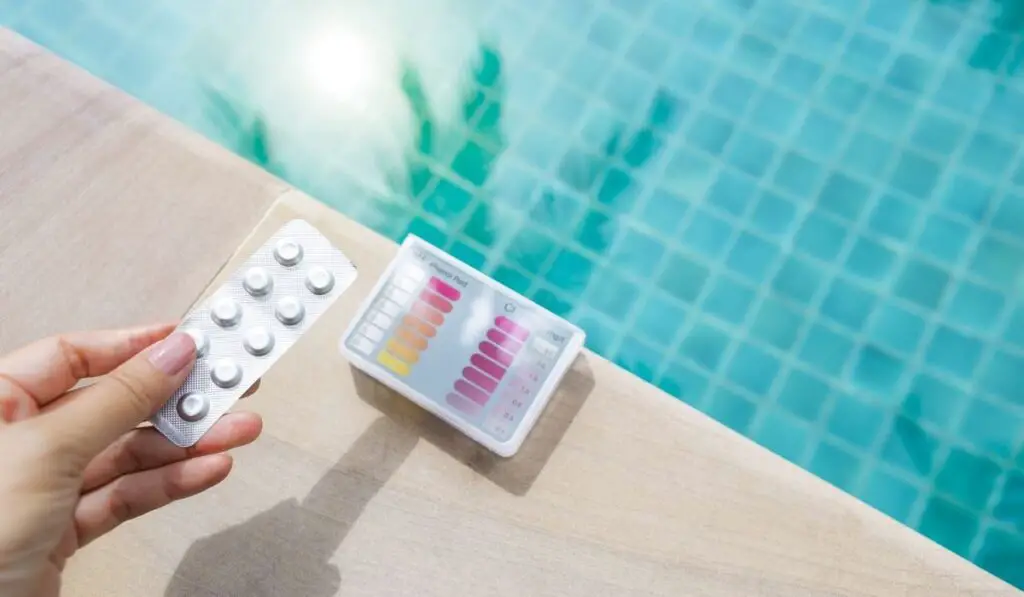 Tablets in girl hand with water testing kit on swimming pool edge with space on blurred clear blue water background