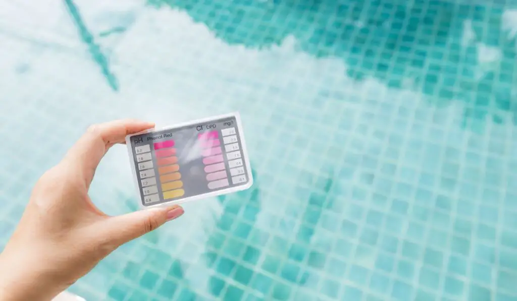 Water testing test kit in girl hand over blurred blue swimming pool water background