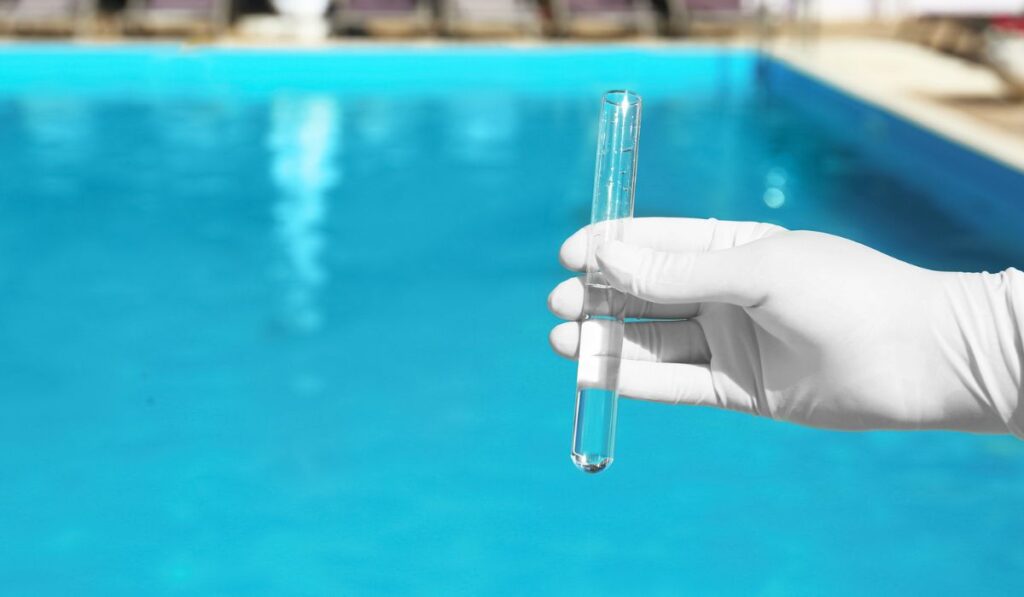 Woman holding glass tube with sample of pool water to check PH level outdoors 