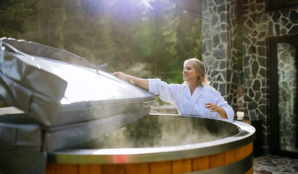 Woman in bathrobe opening lid of hot tub 