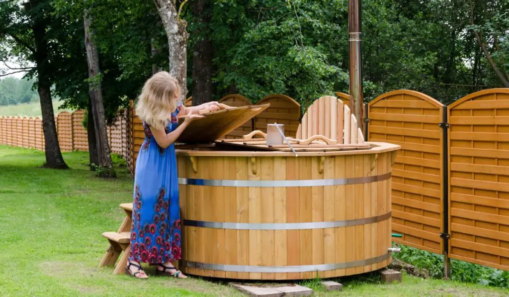 Woman opens water hot tub cover in garden 