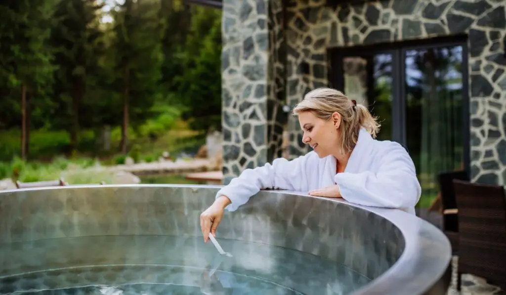 Young woman in bathrobe checking temperature 