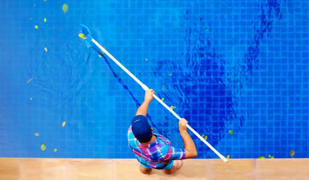 Young adult man personnel cleaning the pool from leaves