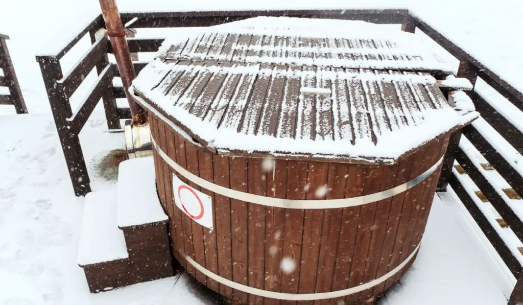 Wooden furaco hot tub stands on the terrace on a snowy winter day