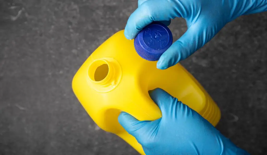 Human hand in protective glove opening a bleach bottle