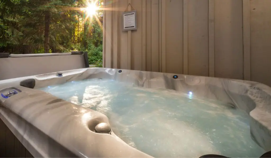 A outdoor hot tub near a forest with a sunburst coming through the trees