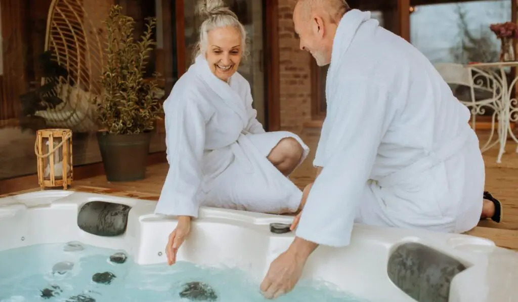 Senior couple in bathrobe checking temperature in outdoor hot tub