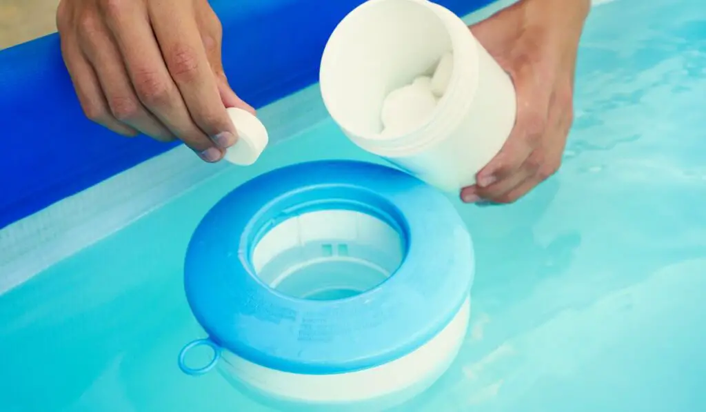 Hand holding white chlorine tablets over swimming pool skimmer