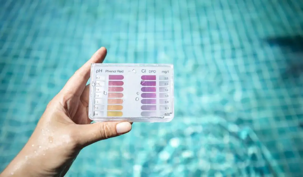 Swimming pool water testing test kit in girl hand over blurred blue water background