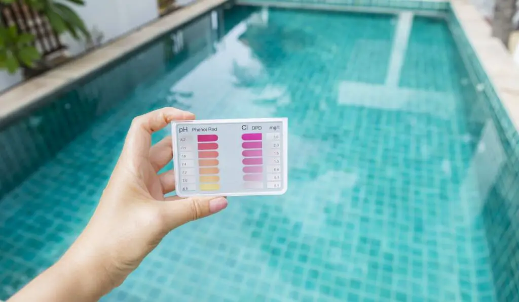 Water testing test kit in girl hand over blurred swimming pool background