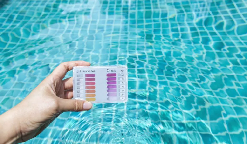 Water testing test kit in girl hand over crystal clear swimming pool water background