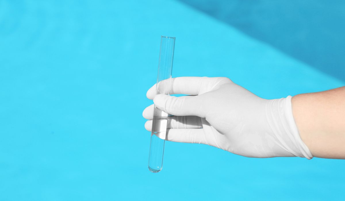 Woman holding glass tube with sample of swimming pool water to check PH level outdoors